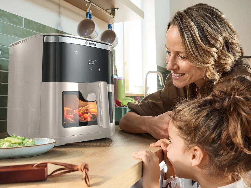 Žena a dievča pozorujú jedlo v teplovzdušnej fritéze Bosch MAF671C0 Serie 6