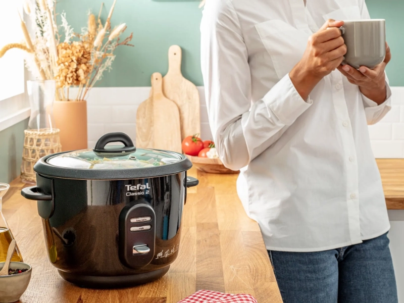 Ryžovar Tefal Classic RK102811 varí a osoba pije kávu