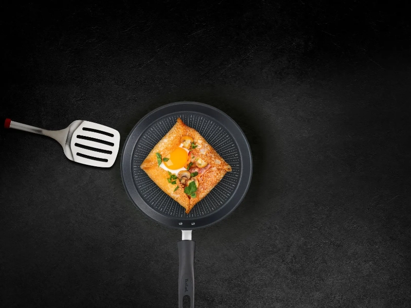 Panvica na palacinky Tefal G2553872 Unlimited 25 cm s obracačkou a palacinkou na čiernom pozadí